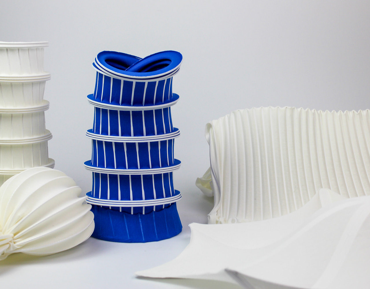 4D-printed textile prototypes: a blue ribbed cylindrical form beside white pleated and folded printed textile pieces.