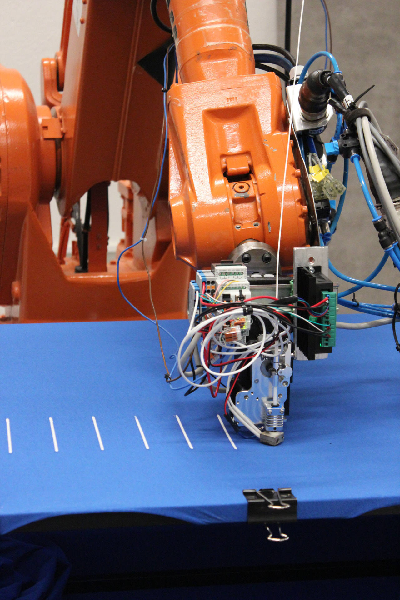 Custom 3D printing extruder mounted on an industrial robot arm in a fabrication lab.